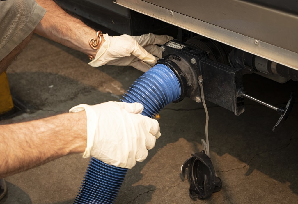 A man's gloved hands connecting hose to RV's holding tanks