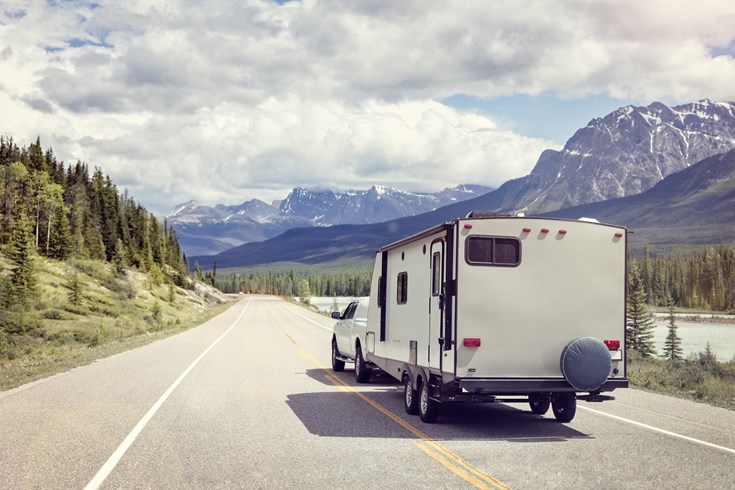 a white pickup truck towing a trailer down an Alaskan highway