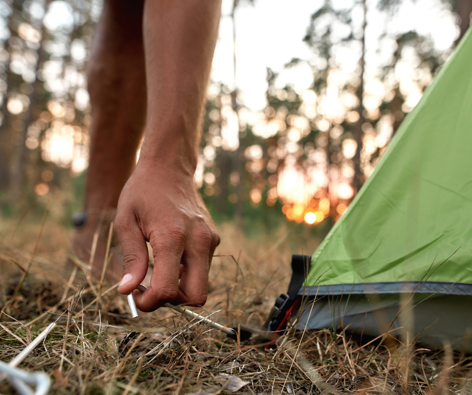 Close up shot of male hand setting up camping tent in forest at sunset. Outdoor adventure, camping trip concept